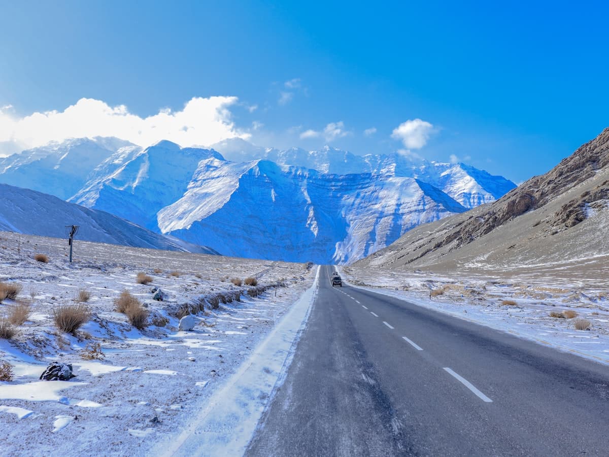 A grey mountain road runs beneath a snow-dusted peak, the kind of bare high pass the Leh-Kargil highway crosses.