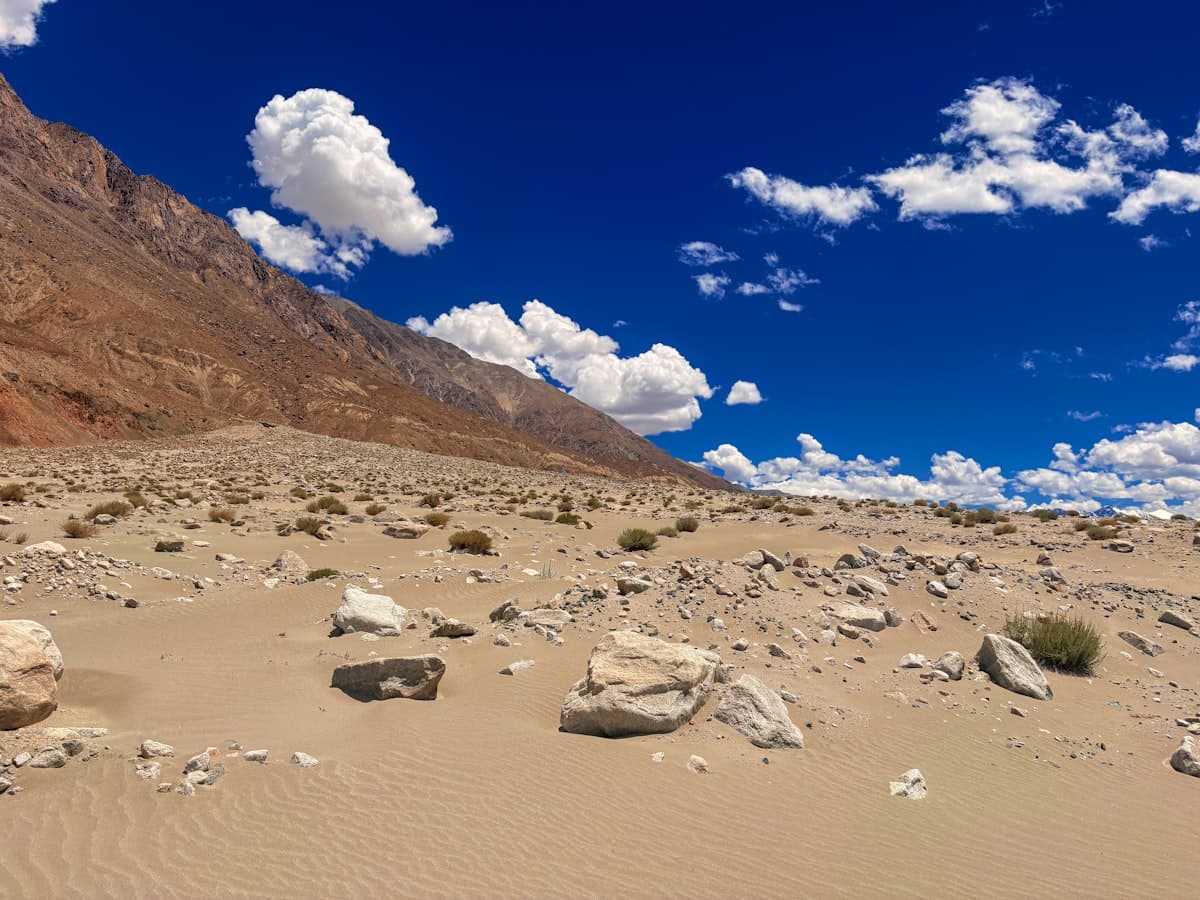 Scattered rock and gravel stretch to distant barren slopes under a hard blue sky — the empty plateau between the two lakes.