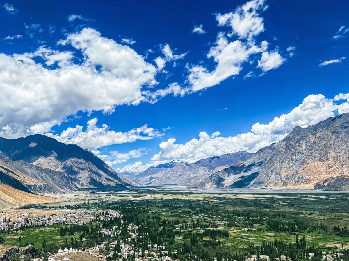 A green terraced settlement of fields and trees sits deep in a valley walled by raw rock ridges.