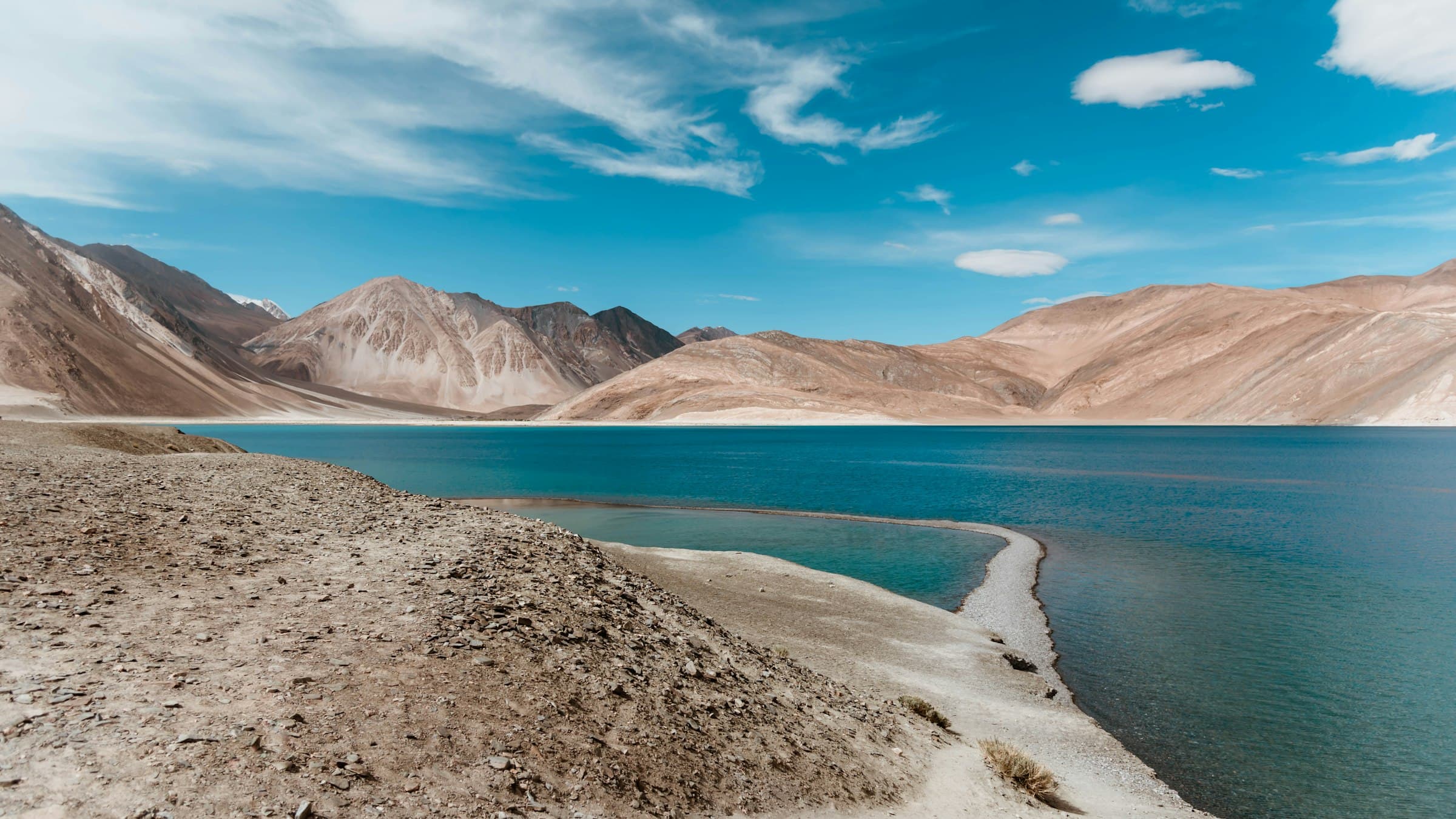 The electric blue water of Pangong Tso stretches between bare ochre mountains under a clear Ladakh sky.