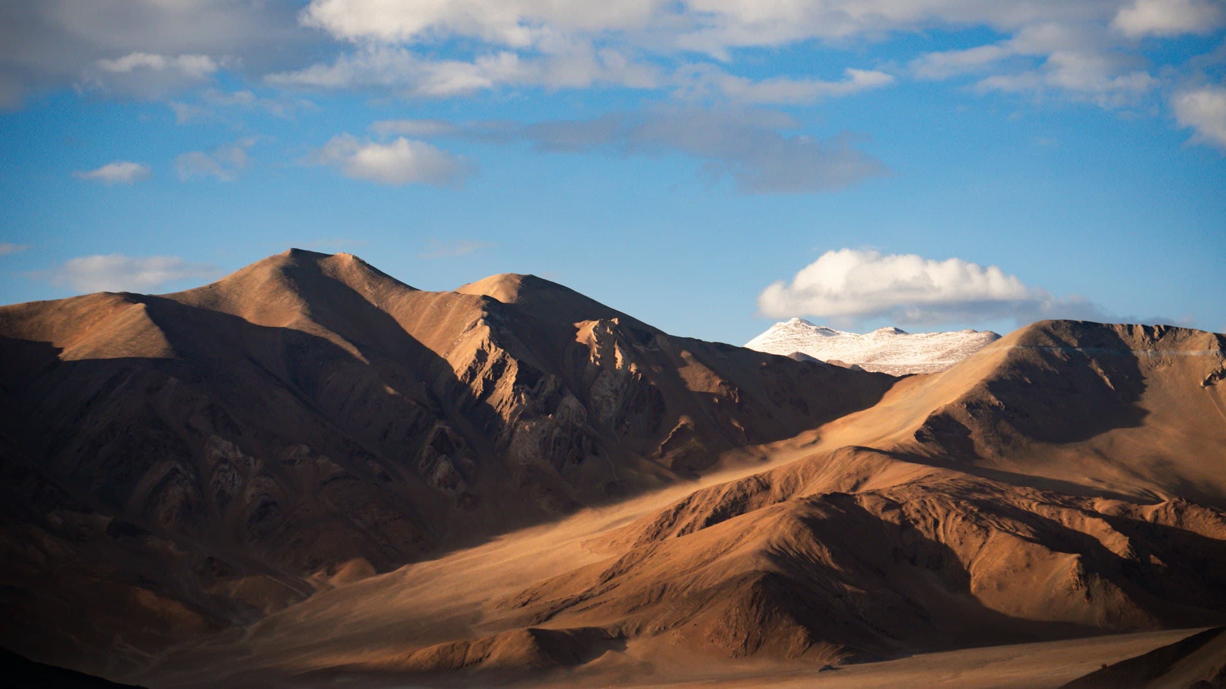Bare Changthang mountains rise straight from the still surface of a vast high-altitude lake on a cloudless day.