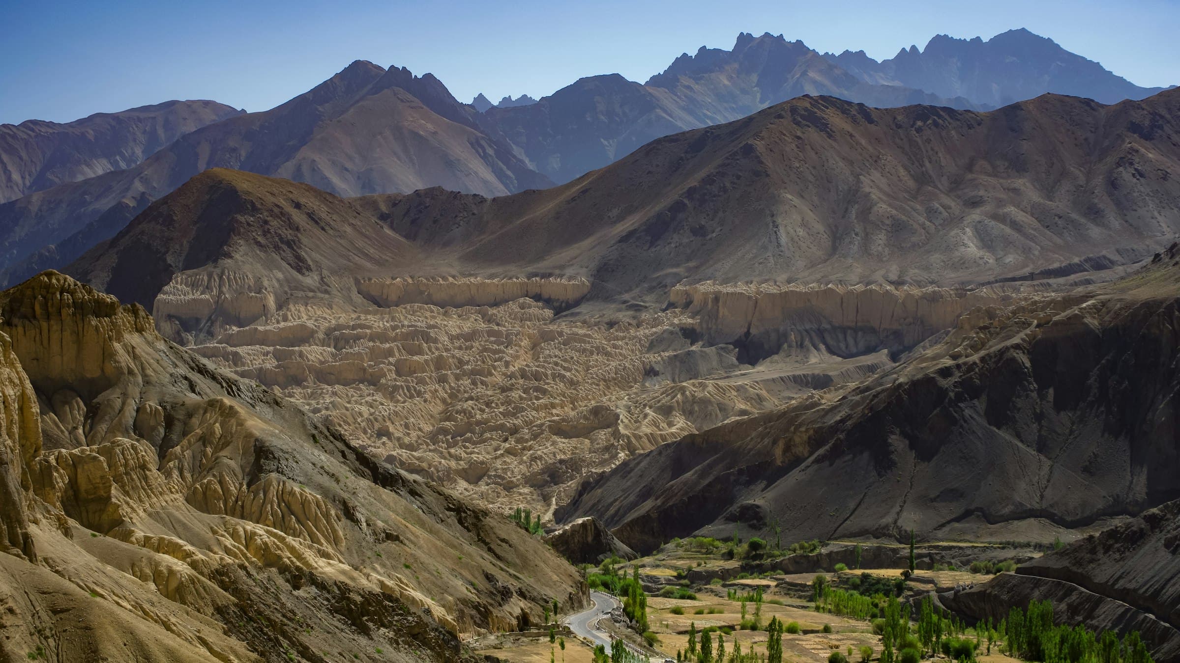 A wide empty valley runs toward successive ranges of bare Ladakhi mountains fading into the distance.