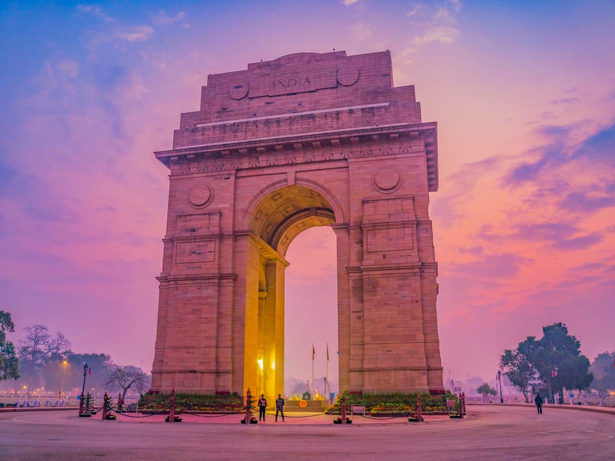 The India Gate war memorial arch rising over Kartavya Path in New Delhi against a deep pink dusk sky.