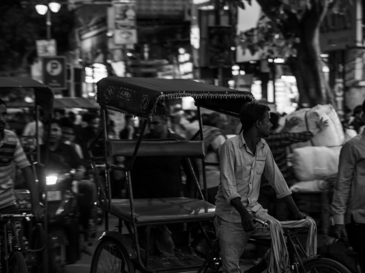 A cycle-rickshaw and its driver threading through crowds in the narrow lanes of Chandni Chowk in Old Delhi.