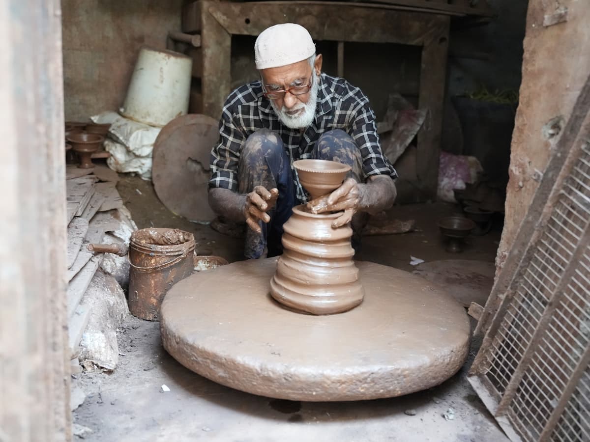 A potter in India shaping a wet clay vessel on a spinning wheel, hands cupped around the rising form.