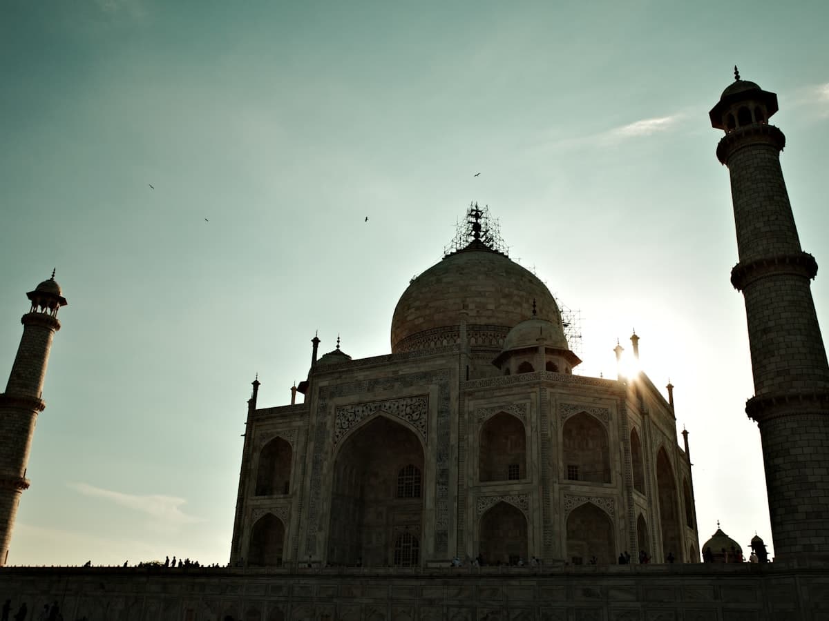 The Taj Mahal's marble mausoleum and flanking minarets standing pale against a bright, near-cloudless early sky.