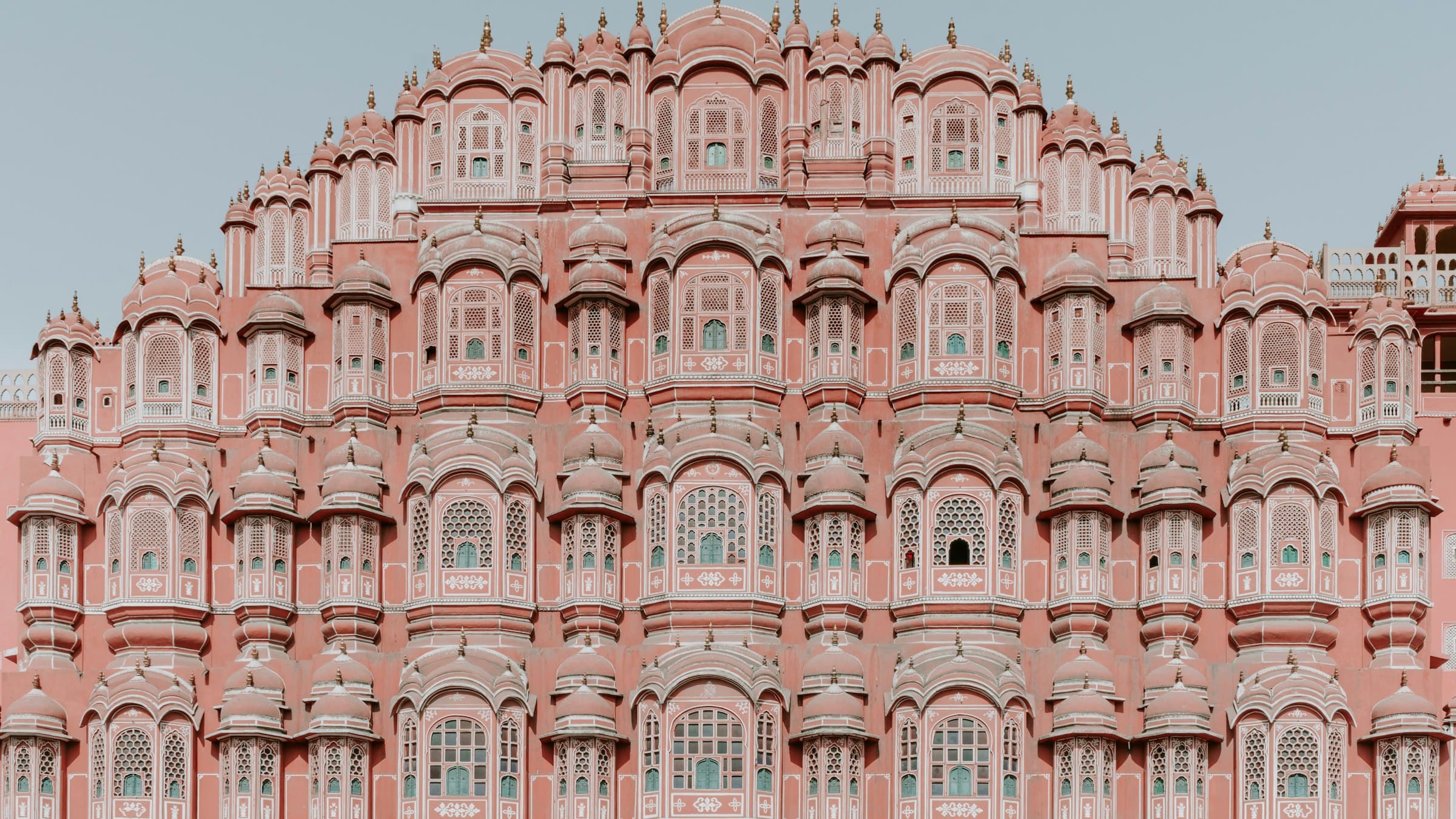 The tiered pink sandstone facade of Jaipur's Hawa Mahal, its honeycomb of latticed jharokha windows rising five storeys.
