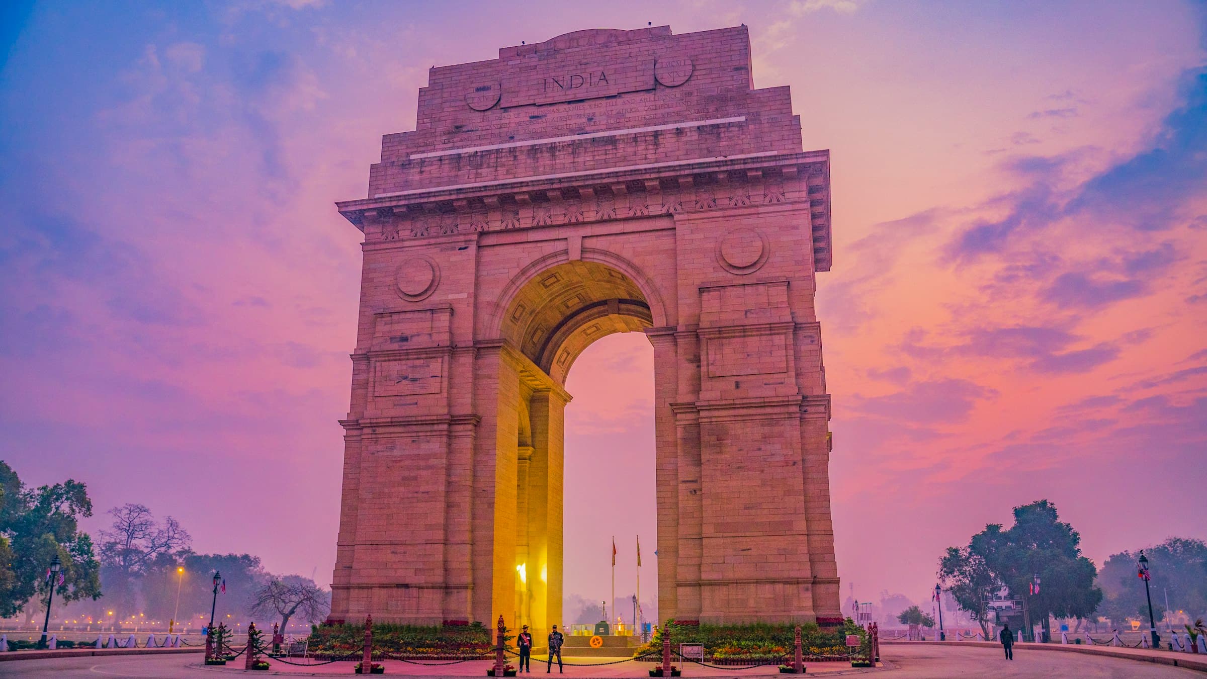 The India Gate war memorial arch on Kartavya Path in New Delhi, silhouetted against a deep pink dusk sky.