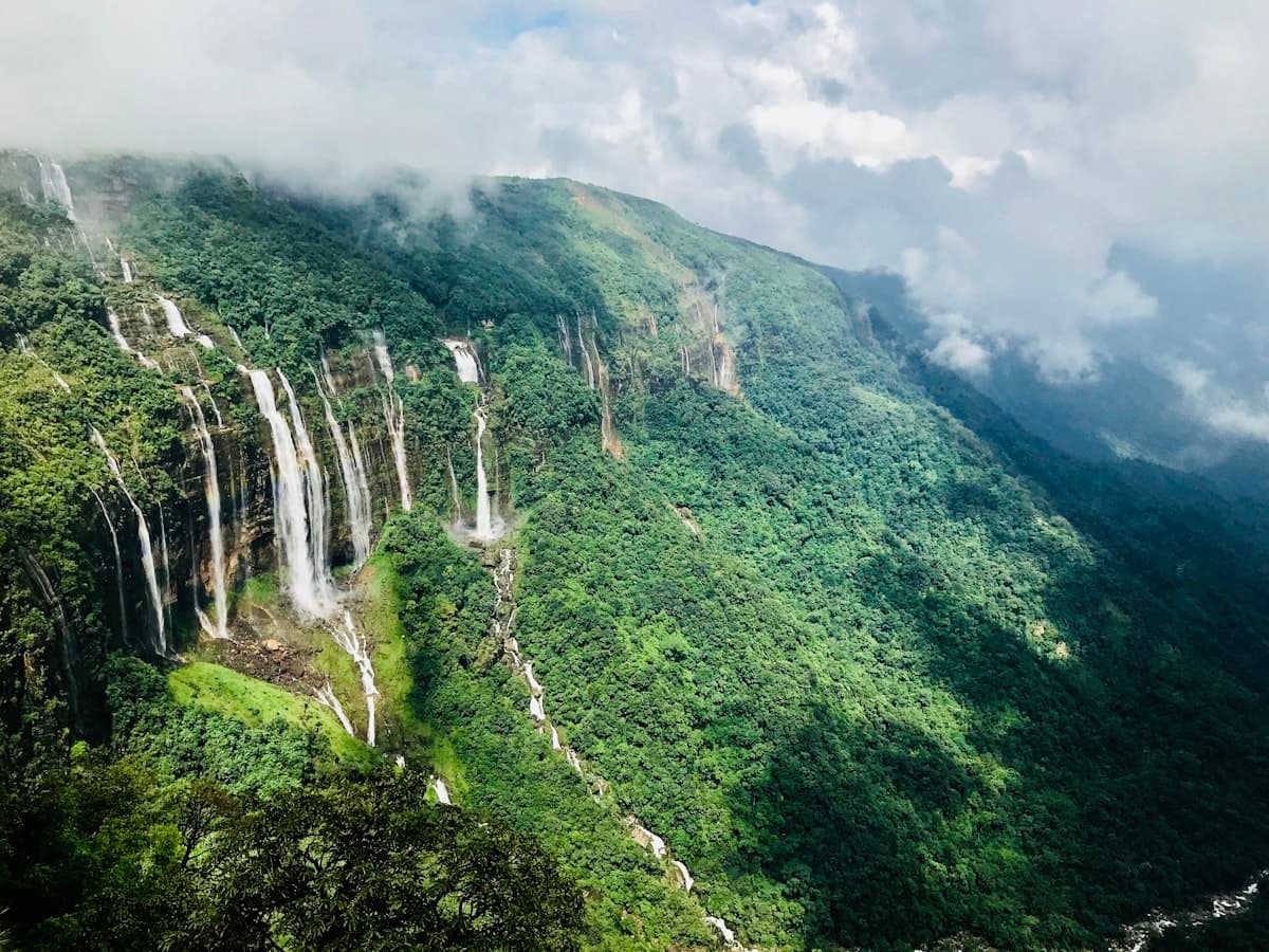 The multi-segmented cascade of Seven Sisters Falls spilling down a green cliff under cloud in Meghalaya.