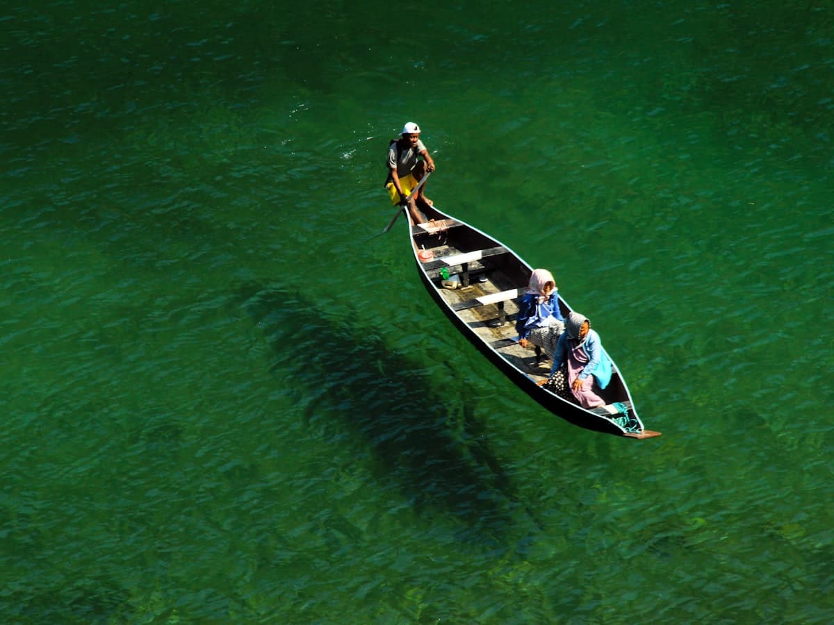 Two people in a small wooden boat on the glass-clear green water of the Umngot River at Dawki, Meghalaya.