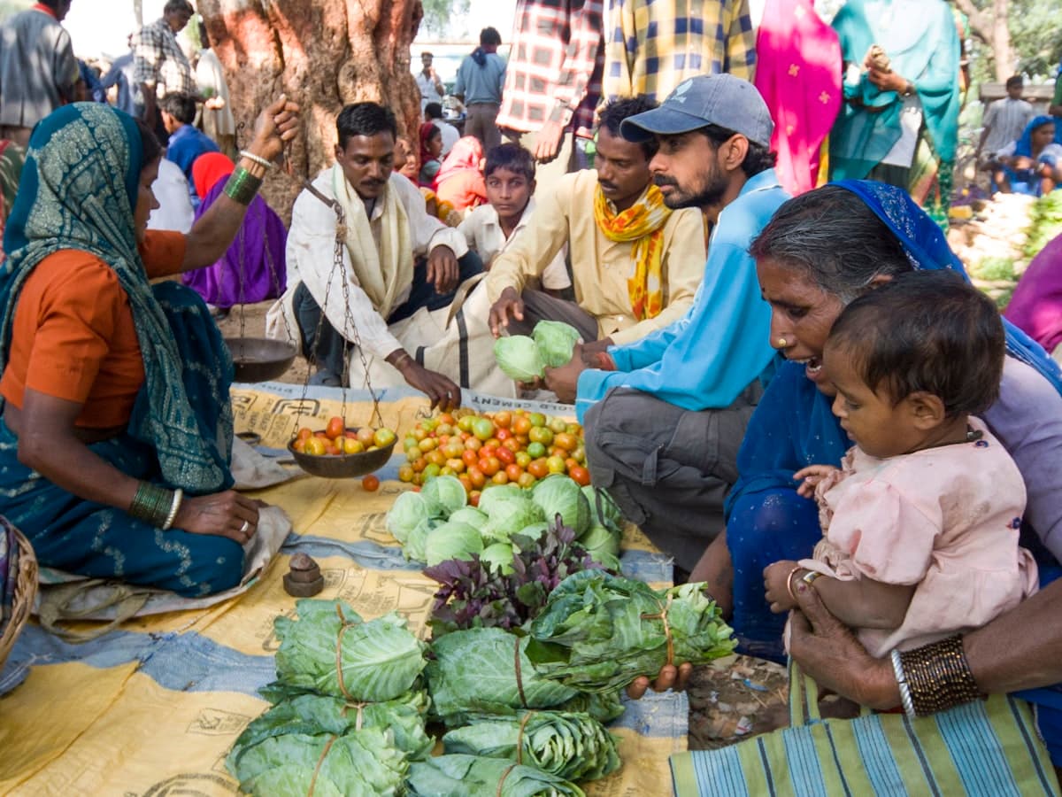 People gathered around baskets of fresh produce at a busy Indian local market.