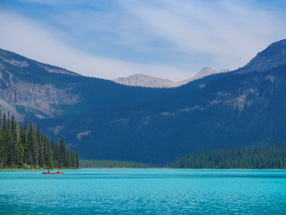 A red canoe on a calm turquoise lake ringed by dense pine forest.