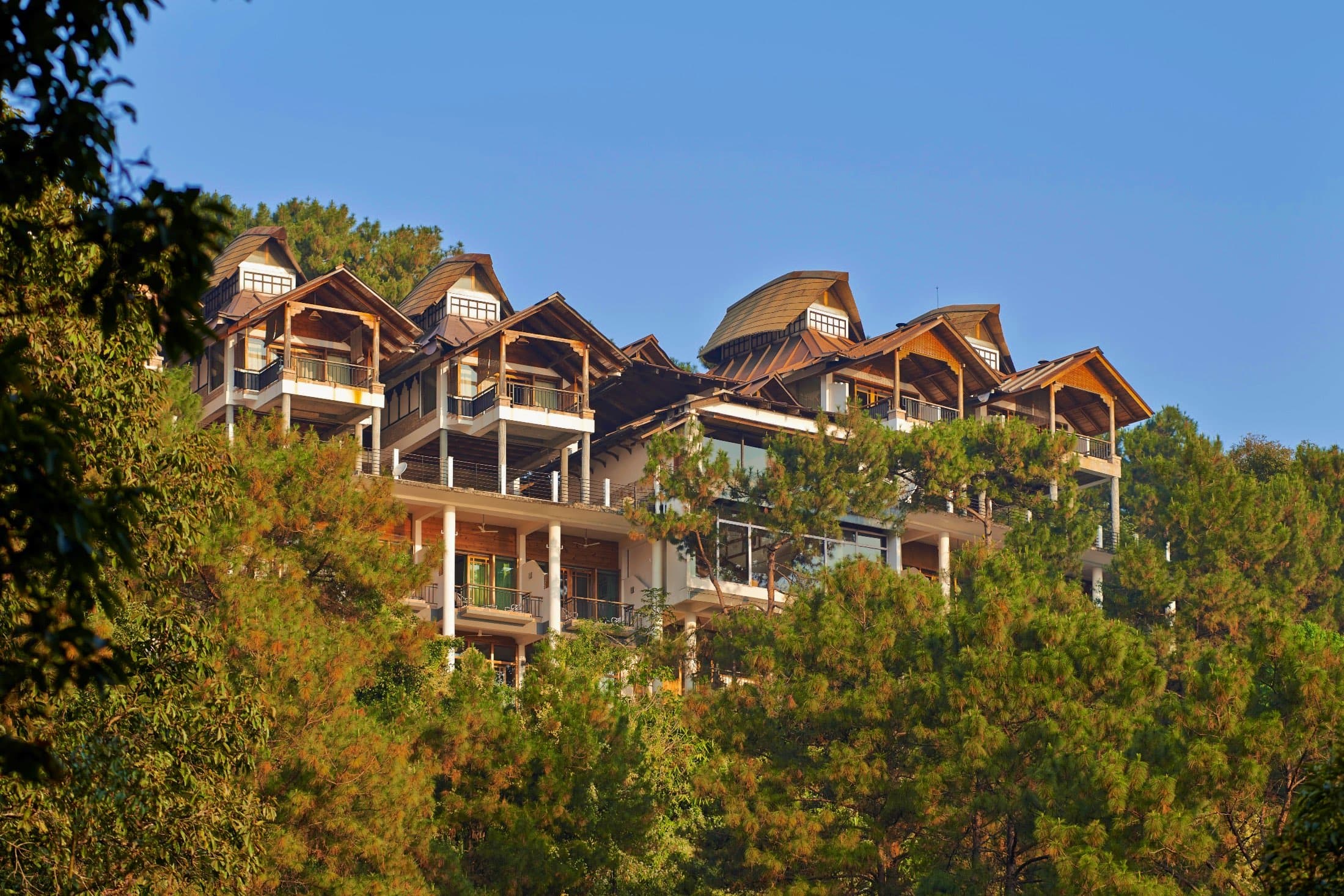 The upturned Khasi boat-roof cottages of Ri Kynjai stepping down a pine-wooded slope above Umiam Lake.