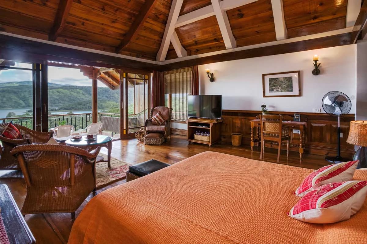 The bed and sitting area of a Ri Kynjai Lake View Cottage under a pitched timber ceiling.