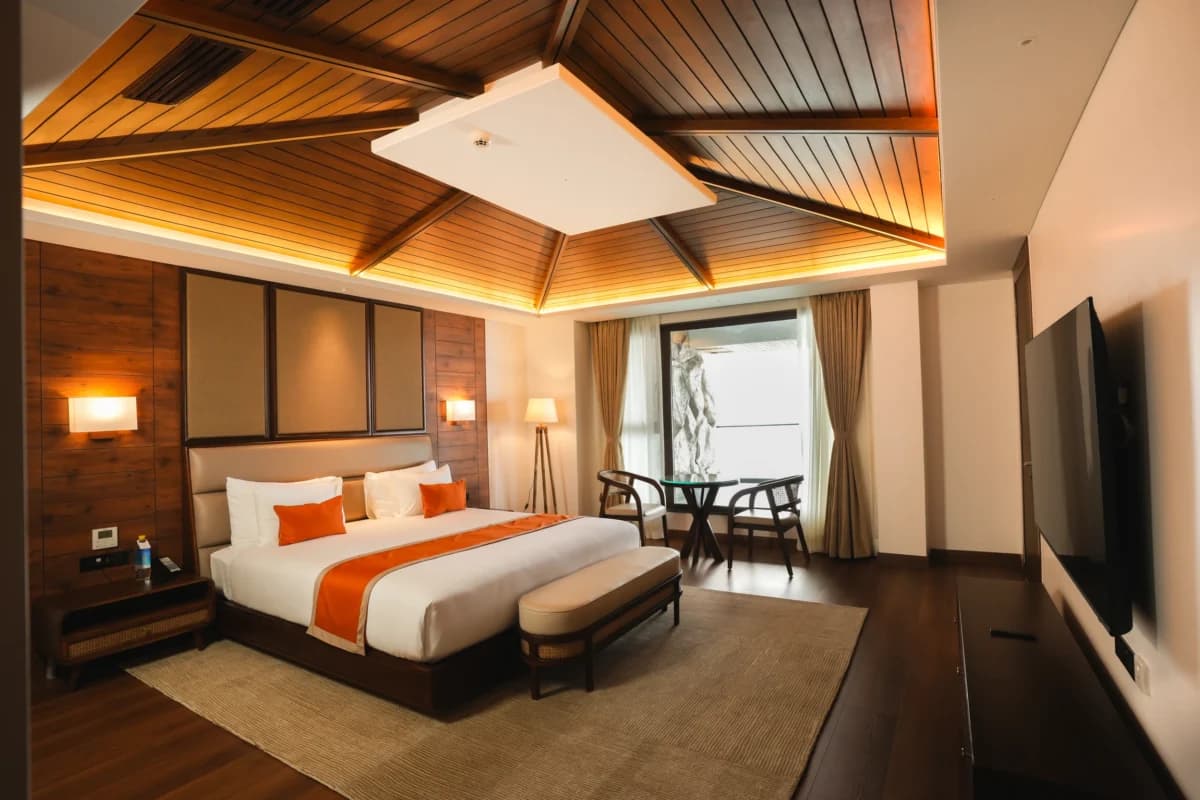 A Horizon Suite bedroom at Jiva Resort, Sohra with an orange-accented bed under a timber-lined ceiling.