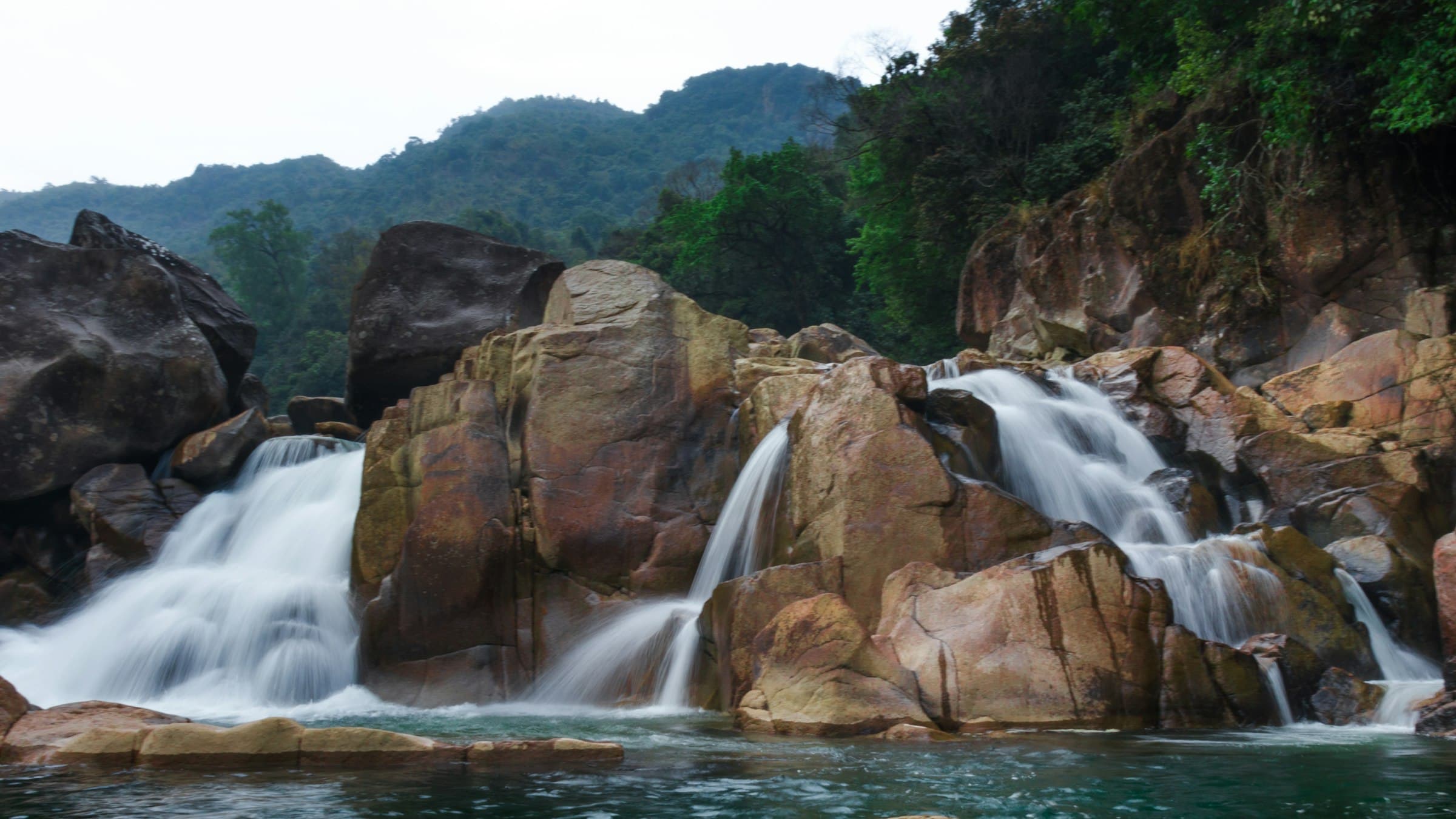 A monsoon waterfall spilling down rocky cliffs into a river in the Jaintia Hills.