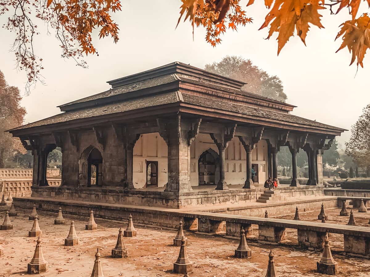 A stone garden pavilion stands among mature trees in a Srinagar garden.
