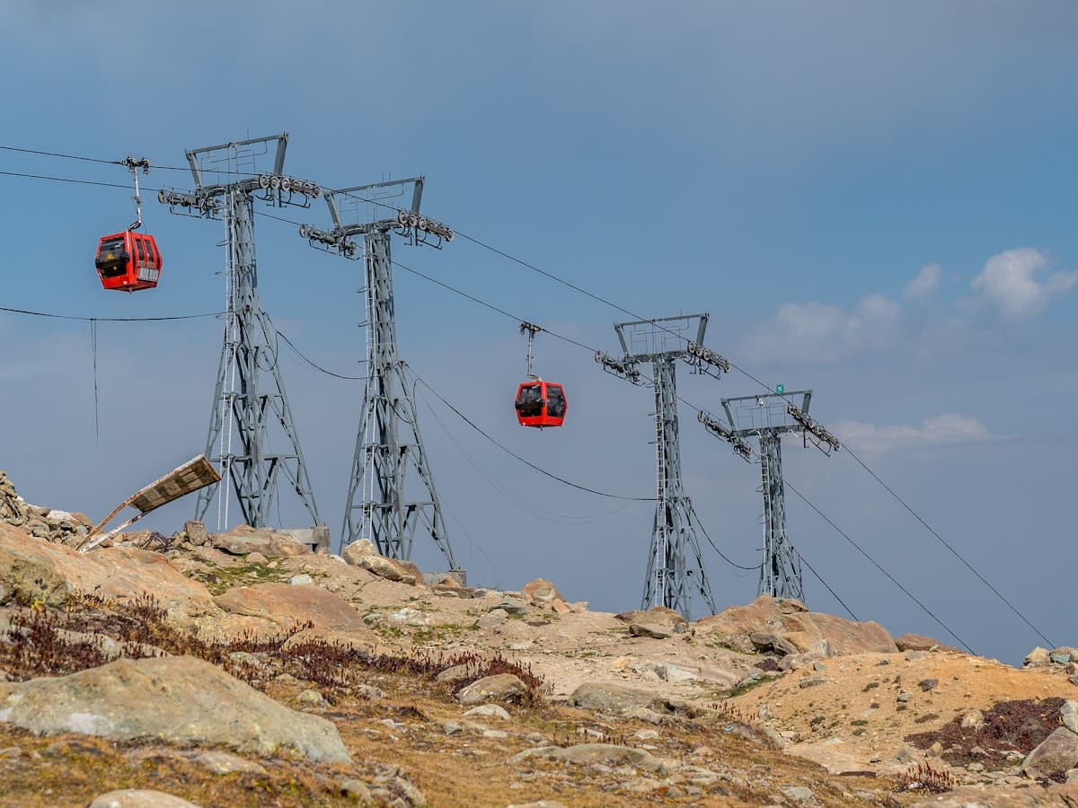 Red gondola cabins climb past cable-car towers on a cloudy mountainside at Gulmarg.