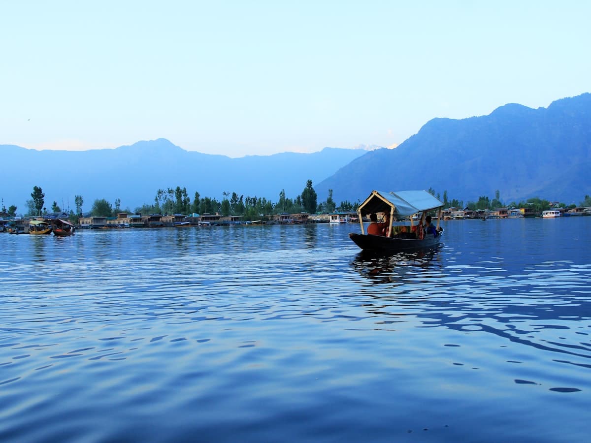 People ride a canopied shikara across Dal Lake toward a tree-lined island.