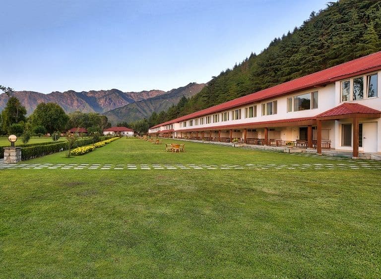 A second exterior view of The LaLiT Grand Palace Srinagar with its lawns and the Zabarwan range behind.