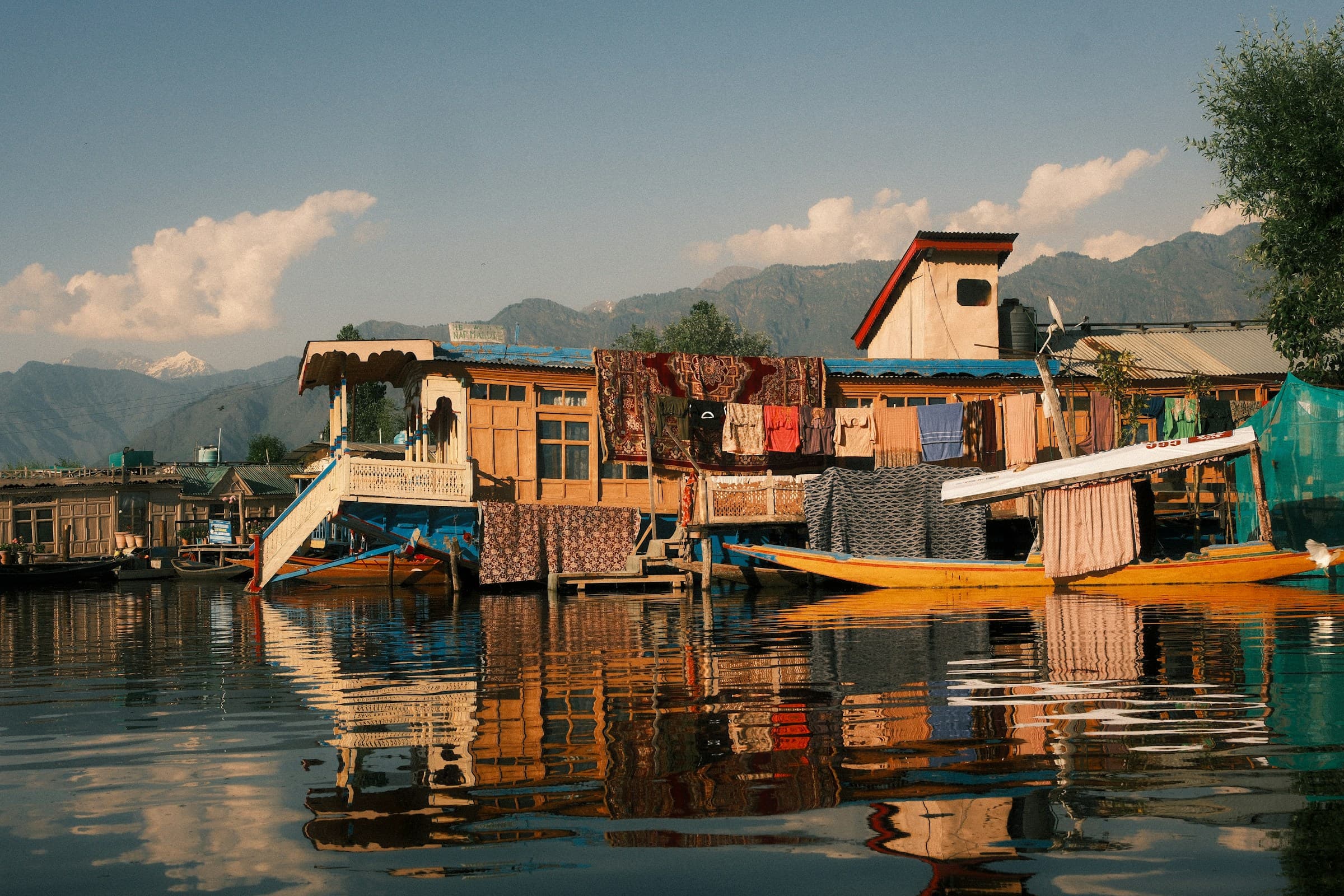 Traditional carved-wood Kashmiri houseboats moored on the calm water of Dal Lake, Srinagar, with distant mountains.