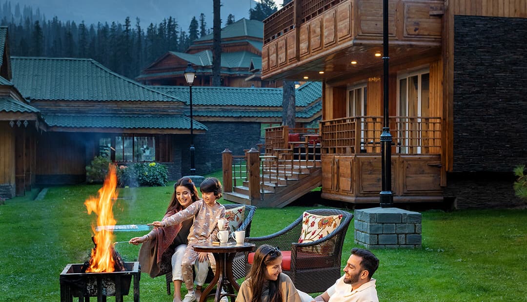 Deodar-and-stone chalets at The Khyber Himalayan Resort & Spa at dusk, with a garden firepit.
