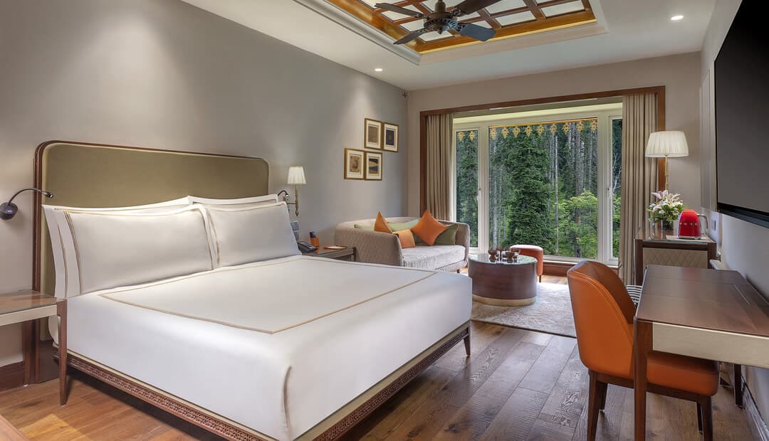 A guest room at The Khyber Himalayan Resort & Spa with a king bed, wood floor and forest-facing windows.