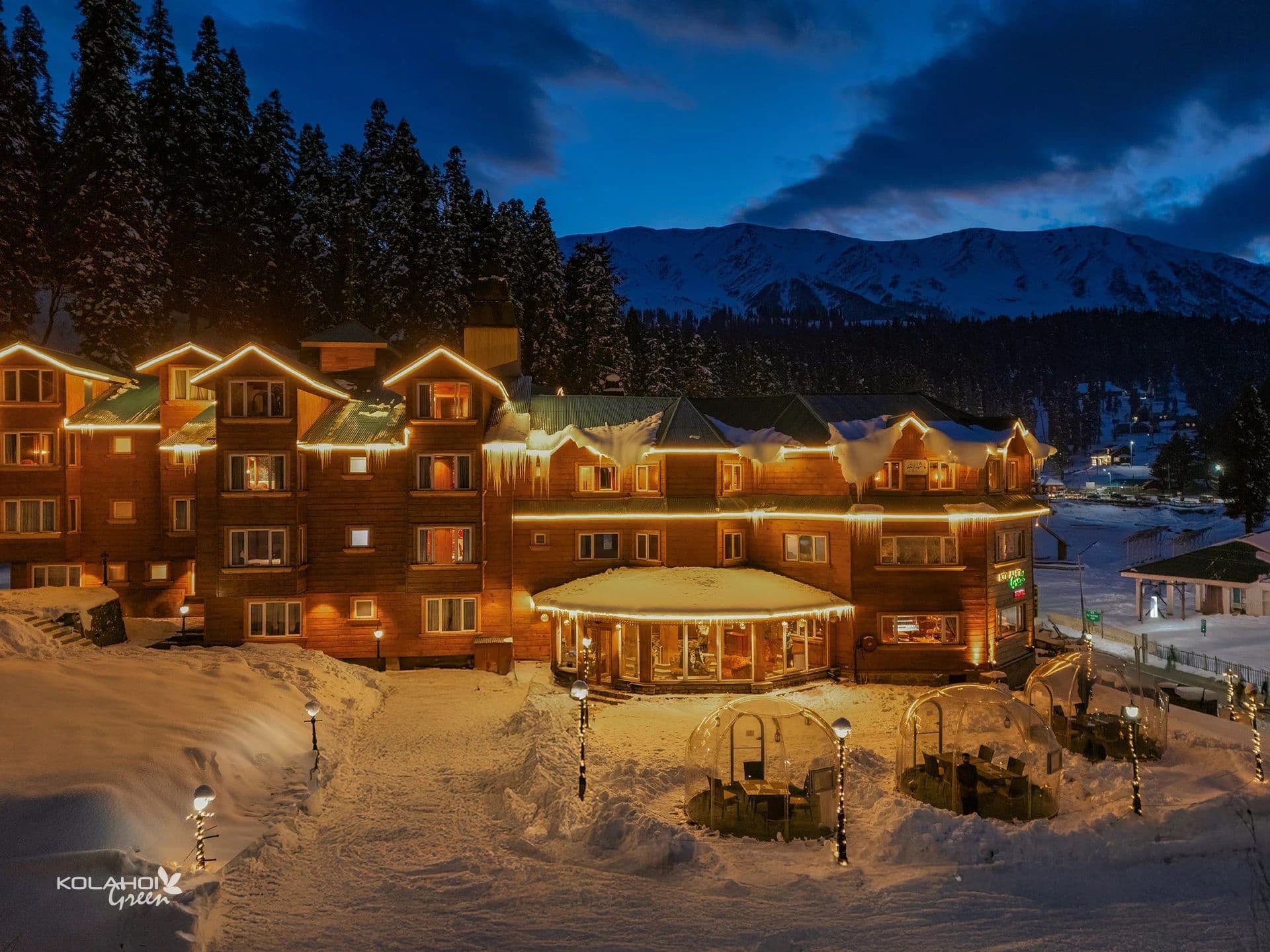 The timber facade of Kolahoi Green Heights, Gulmarg lit up at night against the snow.