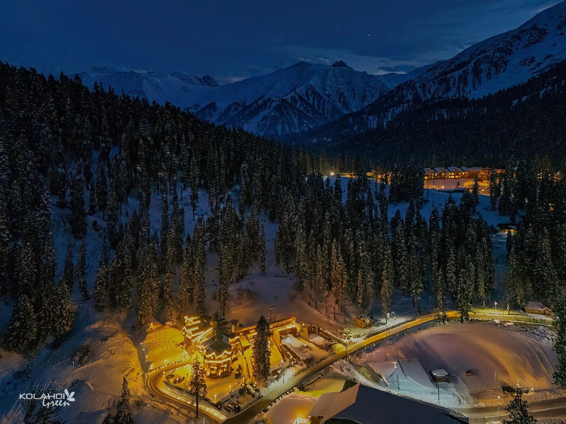 Aerial dusk view of Kolahoi Green Heights and its lit grounds amid the Gulmarg pine forest.