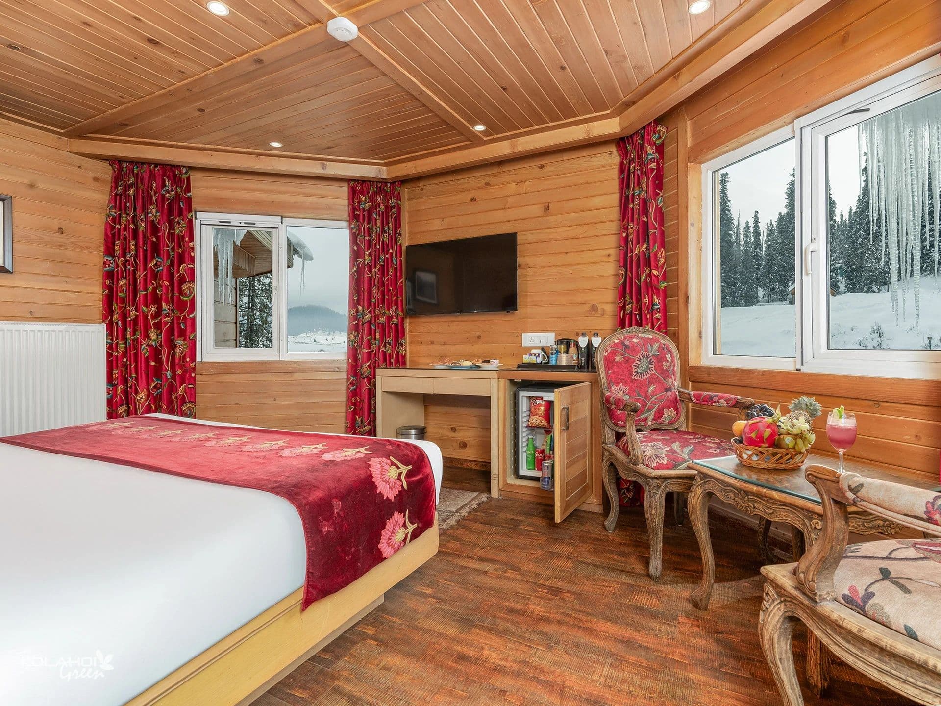A wood-panelled guest room at Kolahoi Green Heights, Gulmarg with red curtains and a seating nook.