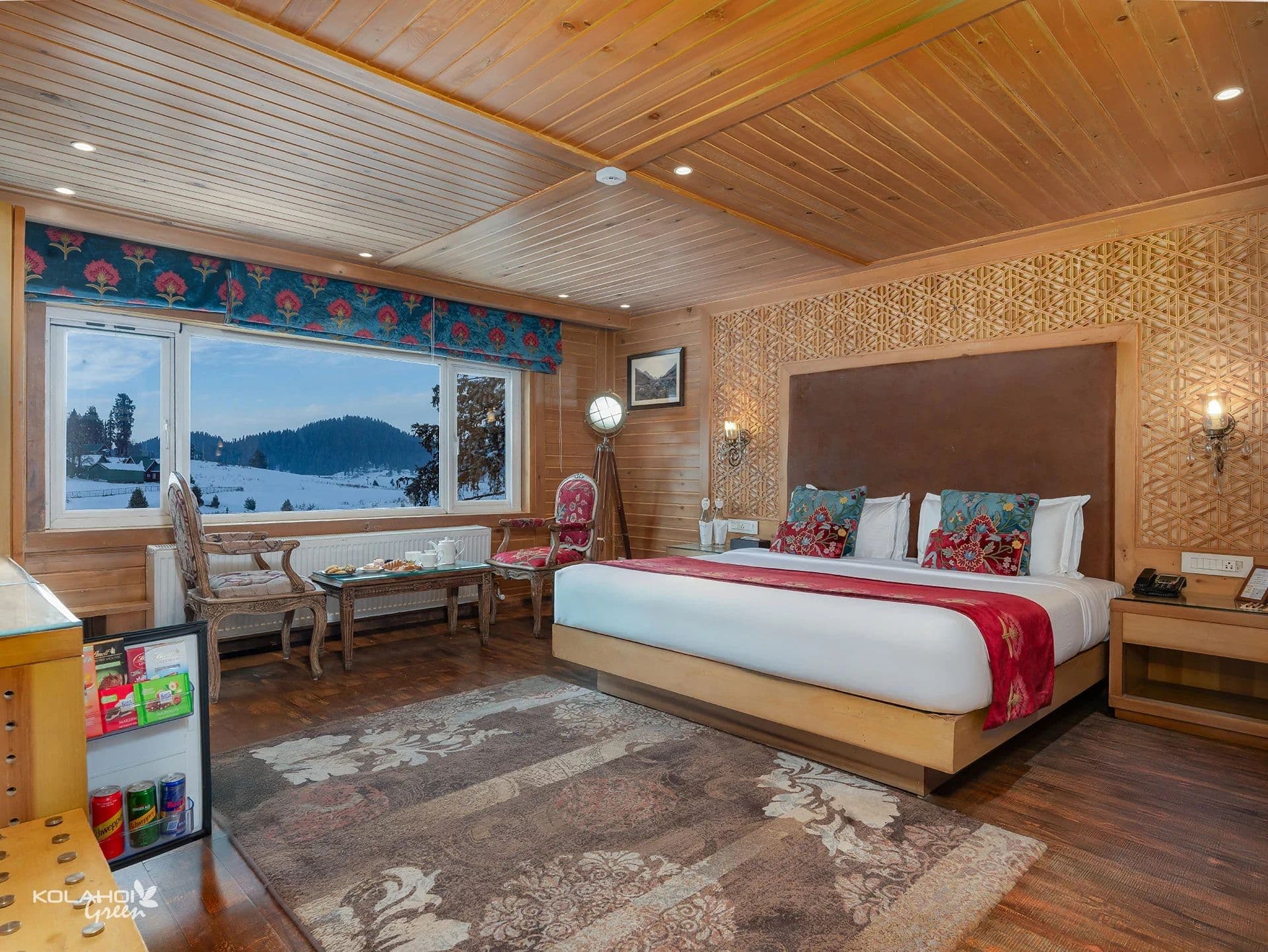 A second guest room at Kolahoi Green Heights, Gulmarg with a padded headboard, rug and window seating.