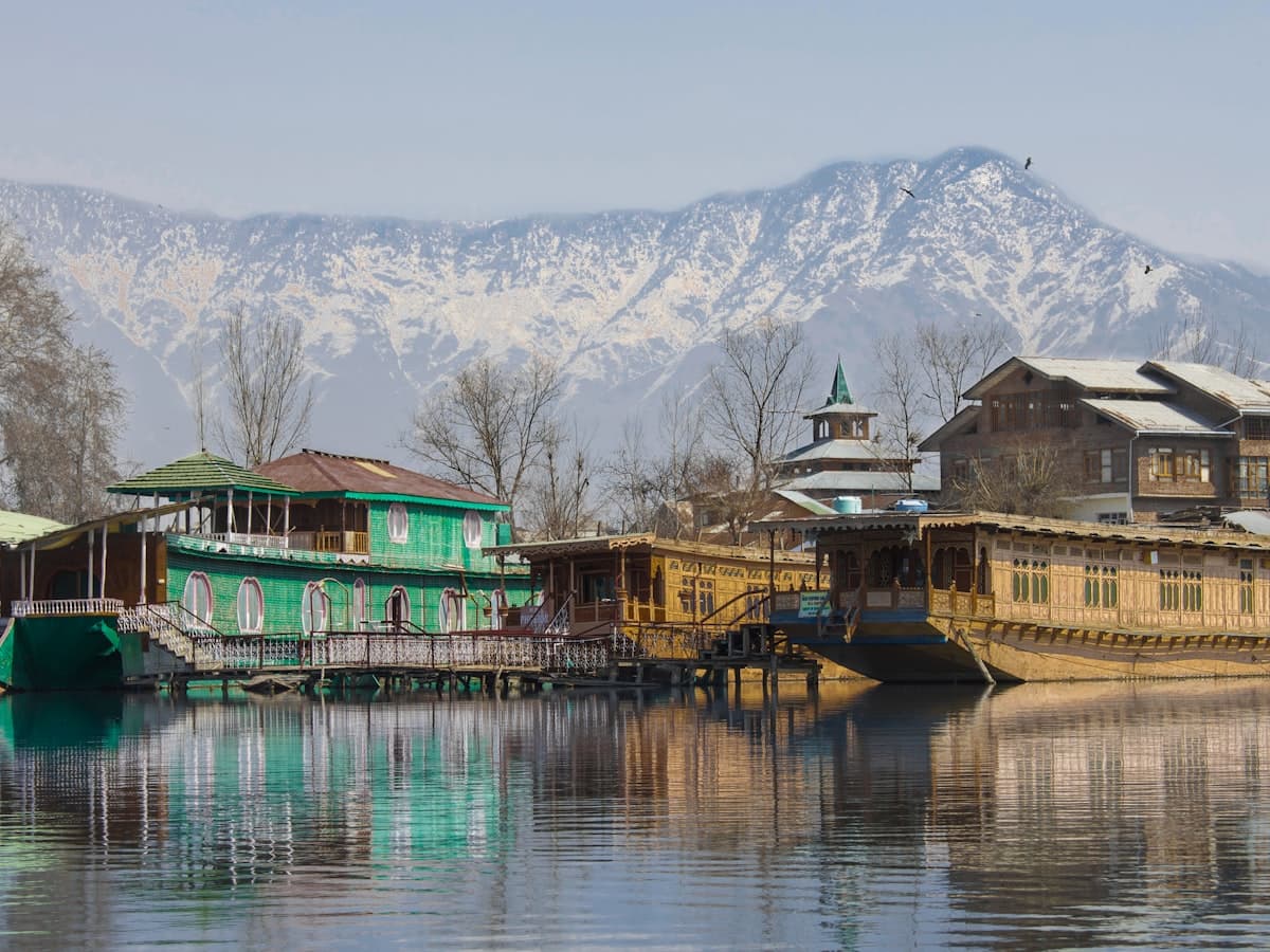 A carved wooden Kashmiri houseboat on Dal Lake below snow-capped mountains.
