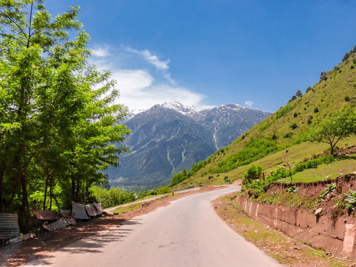 A quiet Kashmir valley road with a roadside bench and mountains.