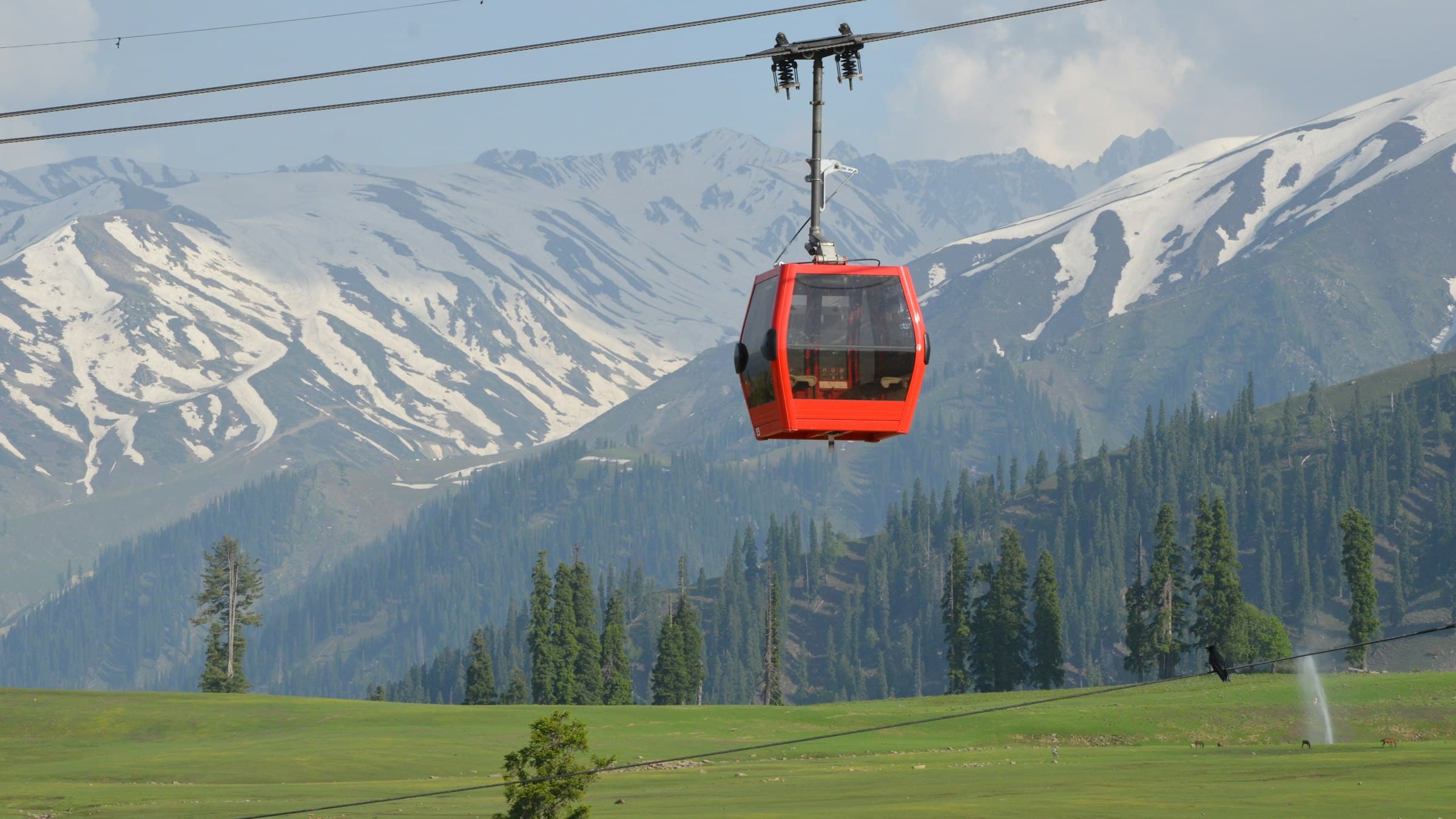 A red Gulmarg gondola cabin rising over snow toward the peaks.