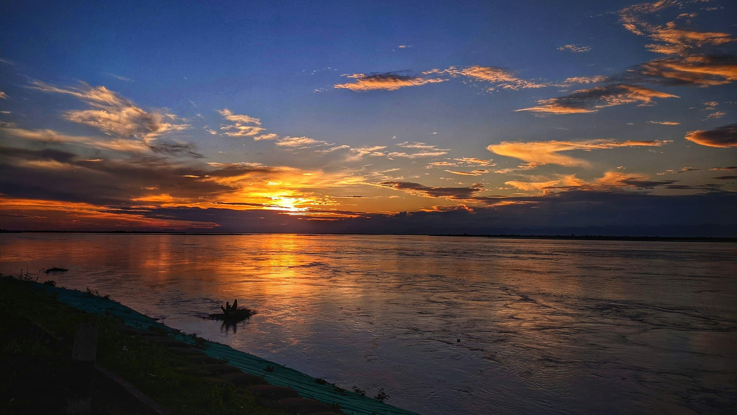 Sunset over the wide Brahmaputra river in Assam, with a jetty silhouetted against a red sky.