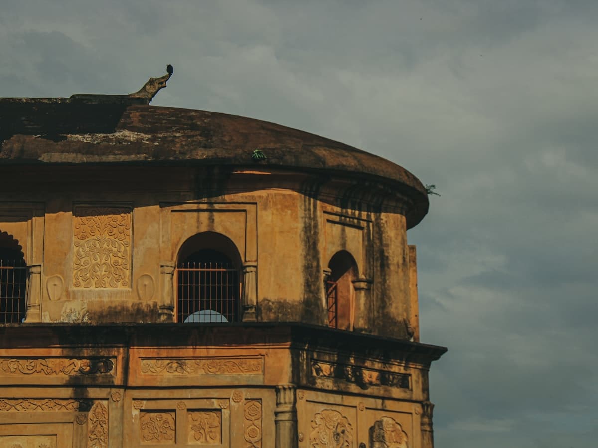 The Rang Ghar, an Ahom-era stone pavilion in Sivasagar, Assam, with a bird perched on its domed roof.