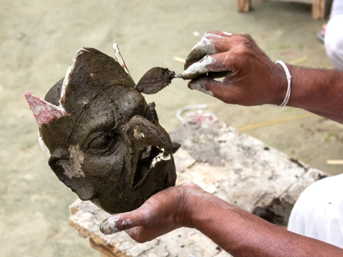 Hands sculpt fine detail into a traditional clay-and-bamboo mask.