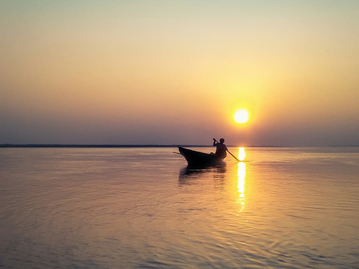 A boatman is silhouetted on the Brahmaputra River at golden hour near Guwahati, Assam.