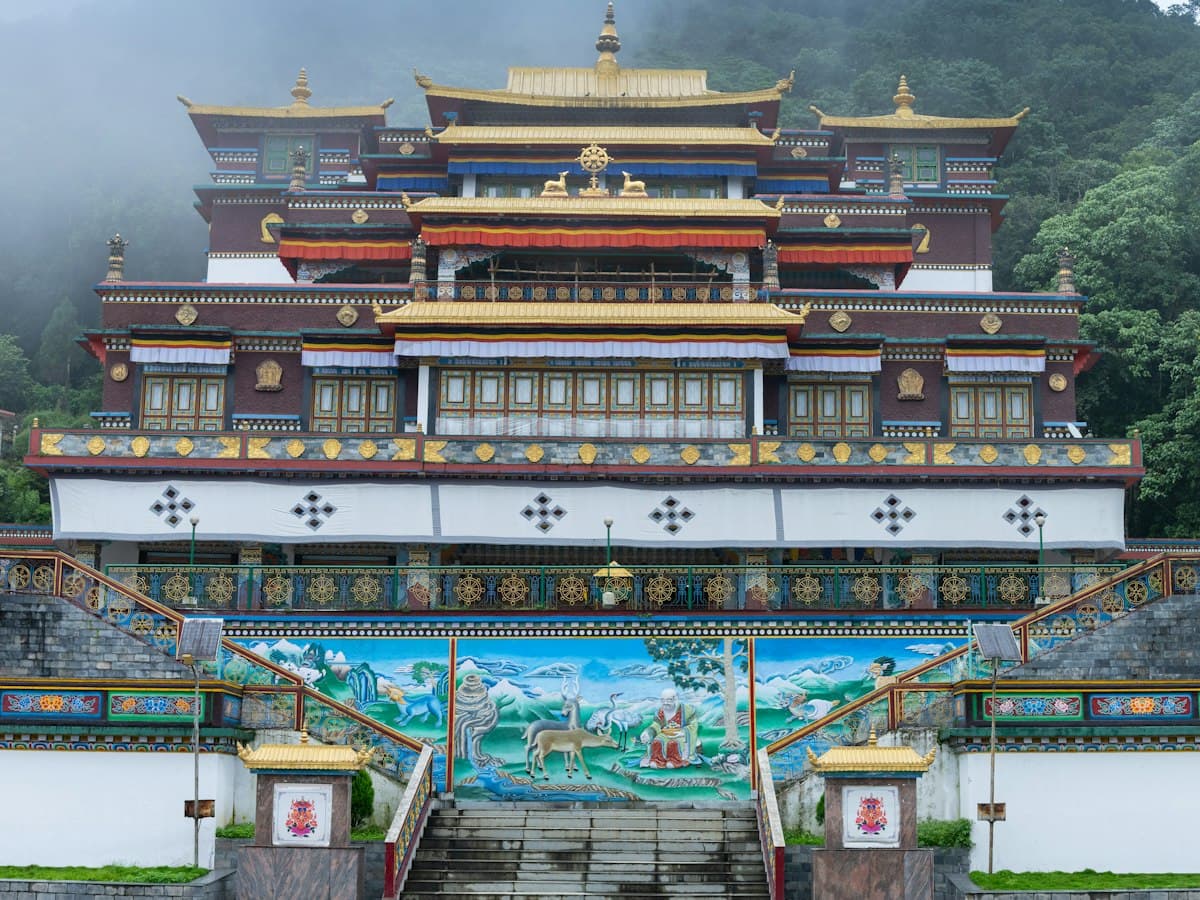 A large Tibetan Buddhist monastery with tiered roofs and gold-topped finials set among the forested hills near Gangtok, Sikkim.