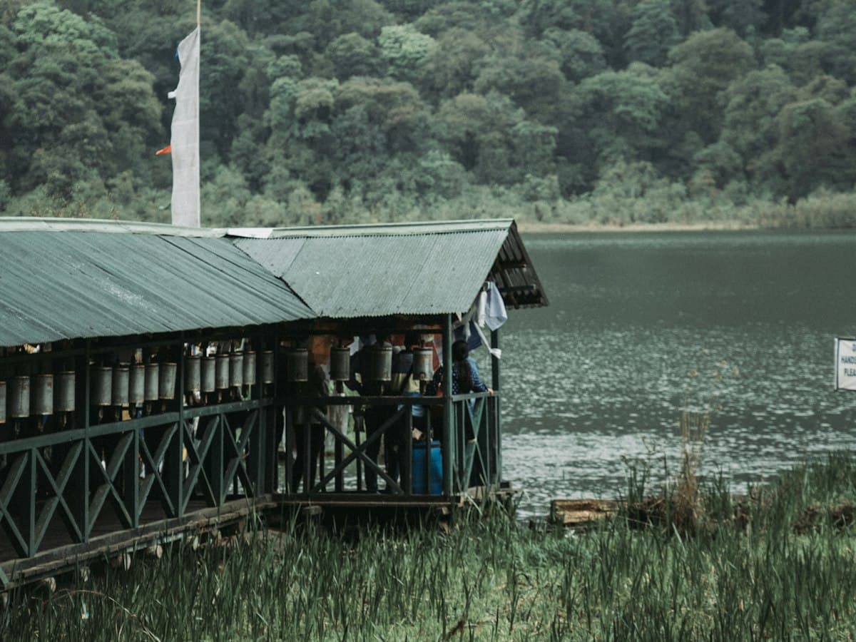 A still forest-ringed lake with a lakeside structure among mountains in Sikkim.