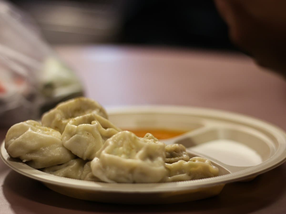 A plate of steamed dumplings (momos) served with a dipping sauce on a table.