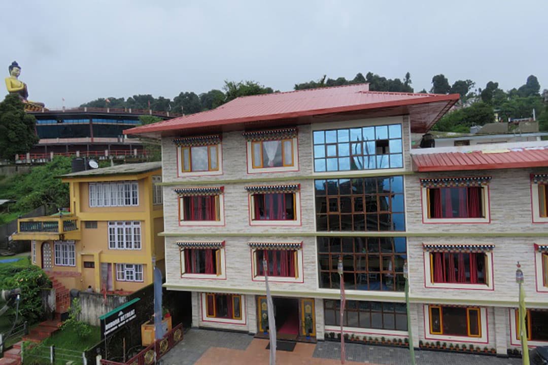 Buddha Retreat's multi-storey building on a Ravangla hillside, with the giant Buddha statue of Buddha Park rising behind it.