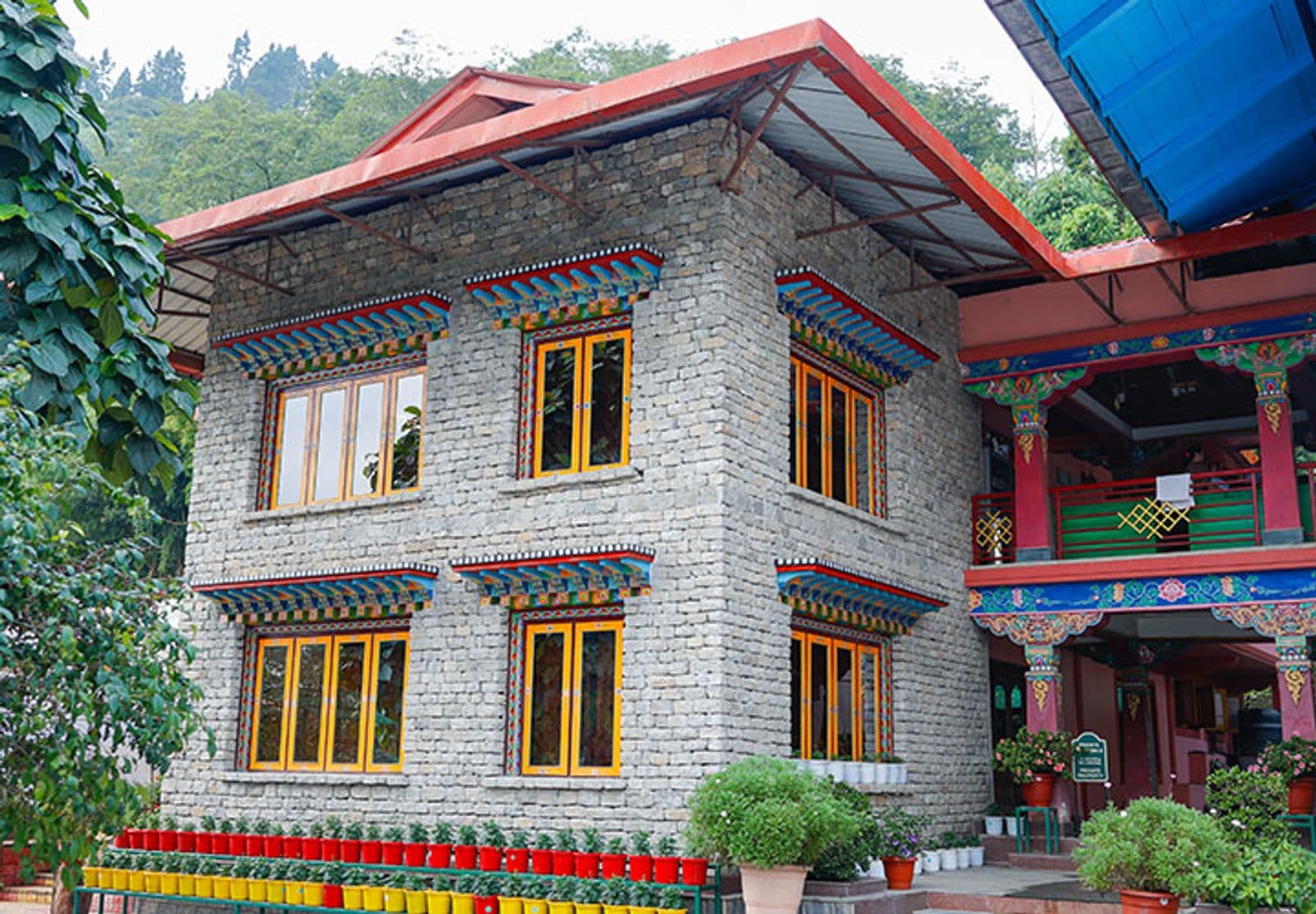 A stone garden cottage with colourful Buddhist eave paintings and potted flowers in the grounds of Buddha Retreat, Ravangla.