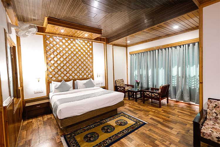 A timber-panelled guest room with a Bhutanese lattice headboard, twin armchairs and a curtained picture window.