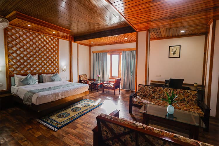 A larger wood-lined room at Buddha Retreat with a lattice headboard, a floral-upholstered sofa and a glass coffee table.