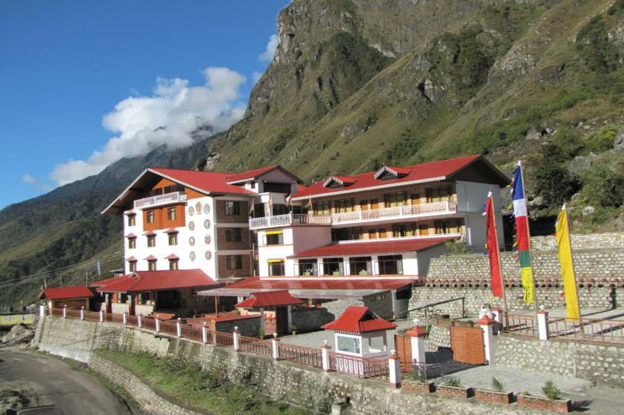 The daytime exterior of Yarlam Resort, Lachung, backed by a rock face and prayer flags.