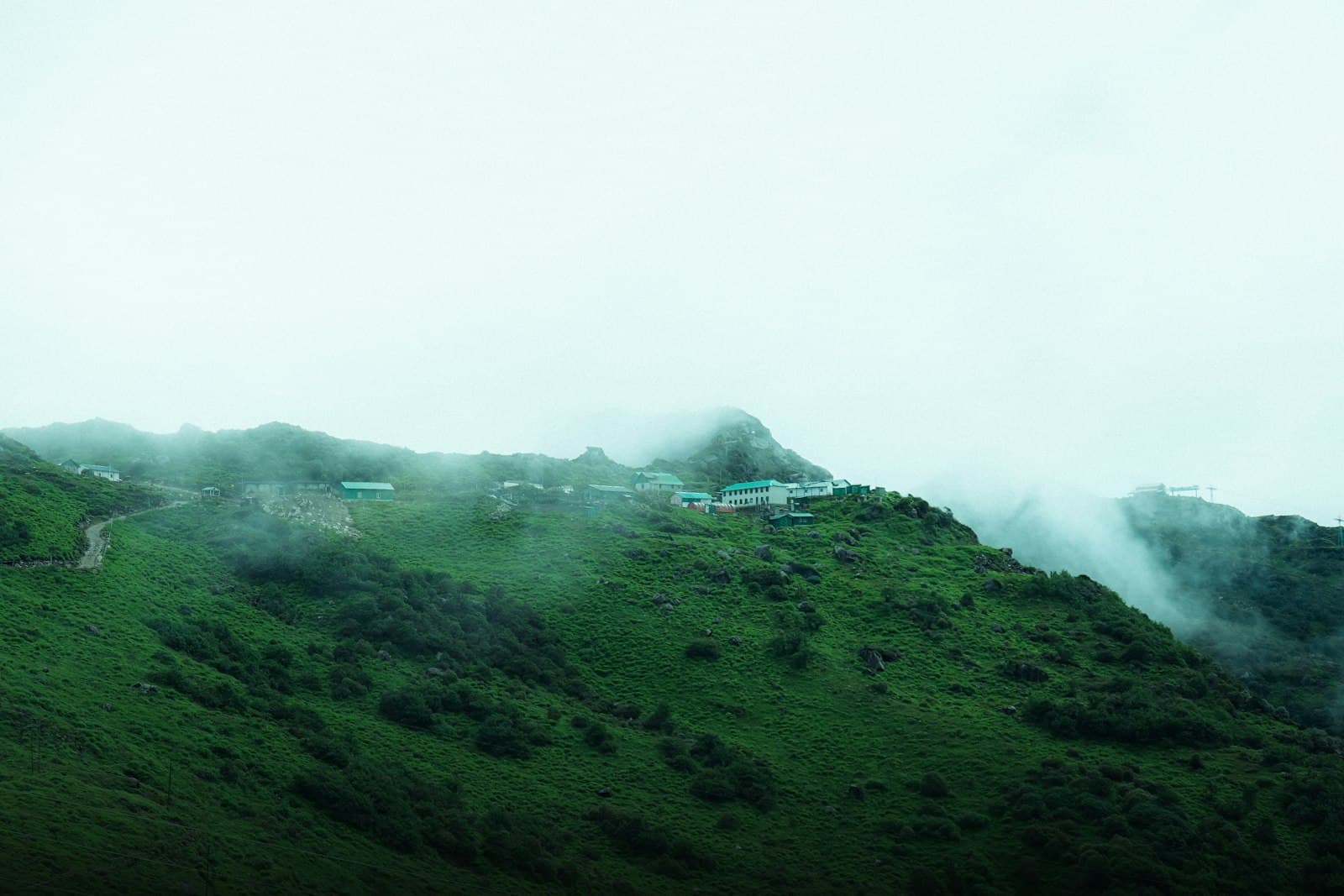 A small cluster of lodge buildings on a mist-covered green Himalayan ridge in North Sikkim.