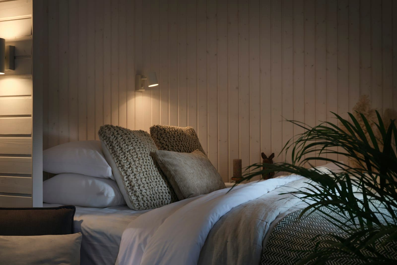 A cosy timber-panelled bedroom with a made-up bed, knitted cushions and a warm reading light.