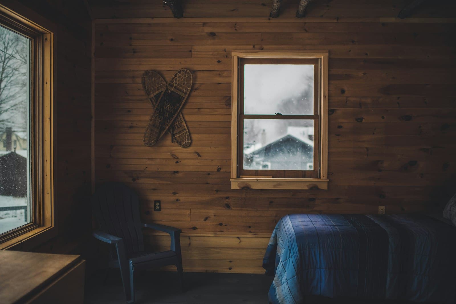 A rustic wood-panelled cabin room with snowshoes on the wall and a window looking onto snow-dusted rooftops.