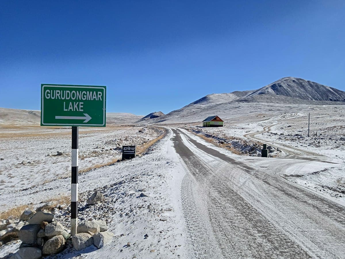 A snow-lined mountain road climbing toward a high-altitude lake in North Sikkim.